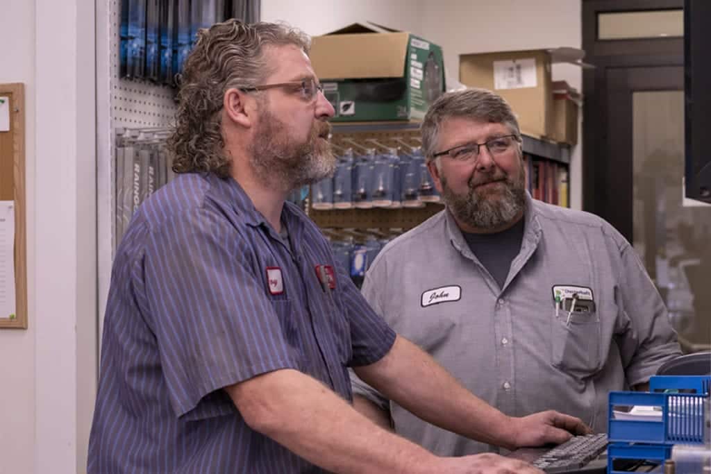 Two auto service technicians stand working at a computer